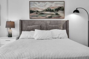 Ein Schlafzimmer mit einem Bett, einem Nachttisch, einer Lampe und einem Bild an der Wand.