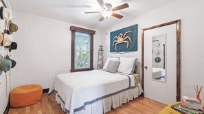 A bedroom with a bed, a ceiling fan, a window with blinds, a wall-mounted mirror, and a door. - Tropical Oasis in Seminole Heights (Tampa)