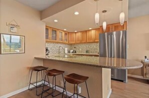 A kitchen with a stainless steel refrigerator, wooden cabinets, a granite countertop, and bar stools. - HUGE SALE!! OCEAN FRONT and BEACH FRONT . Ground floor just steps from the Ocean (Kihei)