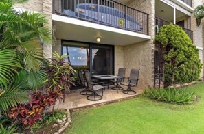 A balcony with outdoor furniture, a stone building facade, and tropical plants. - HUGE SALE!! OCEAN FRONT and BEACH FRONT . Ground floor just steps from the Ocean (Kihei)