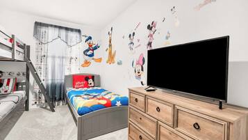 Et børneværelse med køjeseng, fladskærms-tv, kommode og vægdekorationer med Disney-tema.