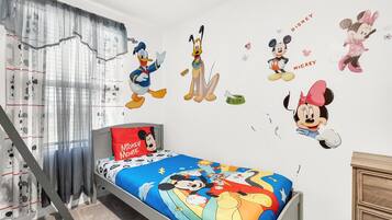 A child's bedroom with Disney-themed wall decals, a bed with a Mickey Mouse pillow, and Mickey Mouse-themed curtains.