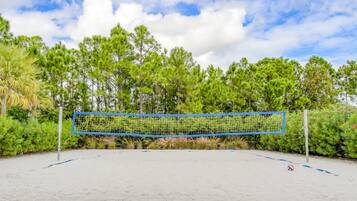 Een volleybalnet op een zandig oppervlak, met op de achtergrond dichte groene bomen en een gedeeltelijk bewolkte lucht.