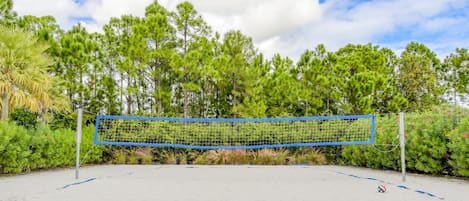 A volleyball net set up on a sandy surface with a backdrop of dense green trees and a partly cloudy sky.