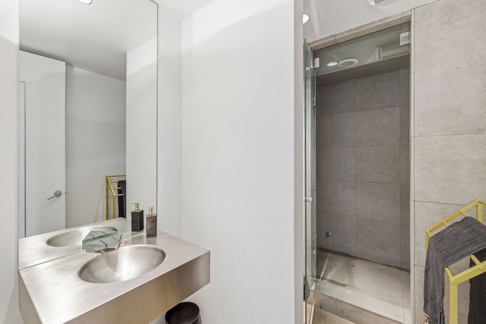 A modern bathroom with a large mirror, two sinks, and a glass-enclosed shower.