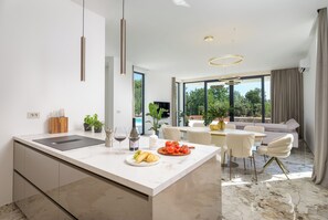 Una cocina moderna con una isla central, comedor con sillas blancas y vista a una piscina.