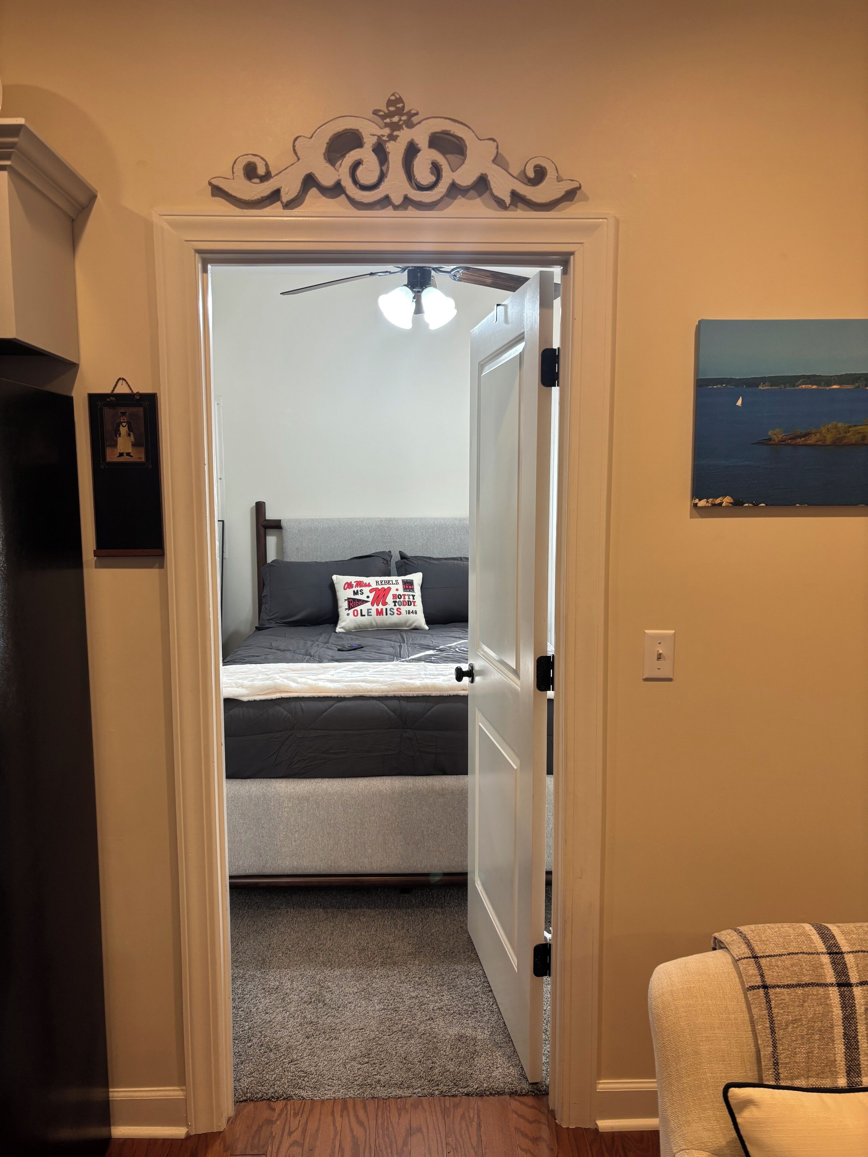 A doorway leading to a bedroom with a bed, a ceiling fan, and a painting on the wall.