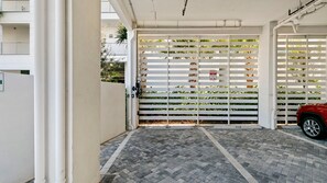 A gated entrance with a paved driveway leading to a red car parked inside. - The Perfect Old Naples Location; Walk to 5th Ave & the Beach! (Naples)