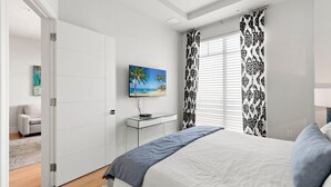 A bedroom with a bed, a TV, a desk, and a door. - The Perfect Old Naples Location; Walk to 5th Ave & the Beach! (Naples)