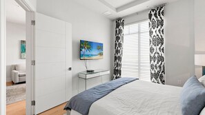 A bedroom with a bed, a TV, a desk, and a door. - The Perfect Old Naples Location; Walk to 5th Ave & the Beach! (Naples)