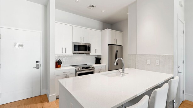 A modern kitchen with white cabinetry, stainless steel appliances, and a central island with seating. - The Perfect Old Naples Location; Walk to 5th Ave & the Beach! (Naples)