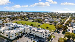 A residential area with a large building featuring multiple floors, a parking lot, and a green space with a sports field. - The Perfect Old Naples Location; Walk to 5th Ave & the Beach! (Naples)