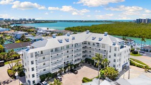 A multi-story hotel with a central courtyard, surrounded by palm trees and a view of the ocean.
