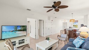 A living room with a television, a ceiling fan, and a dining area with a table and chairs.