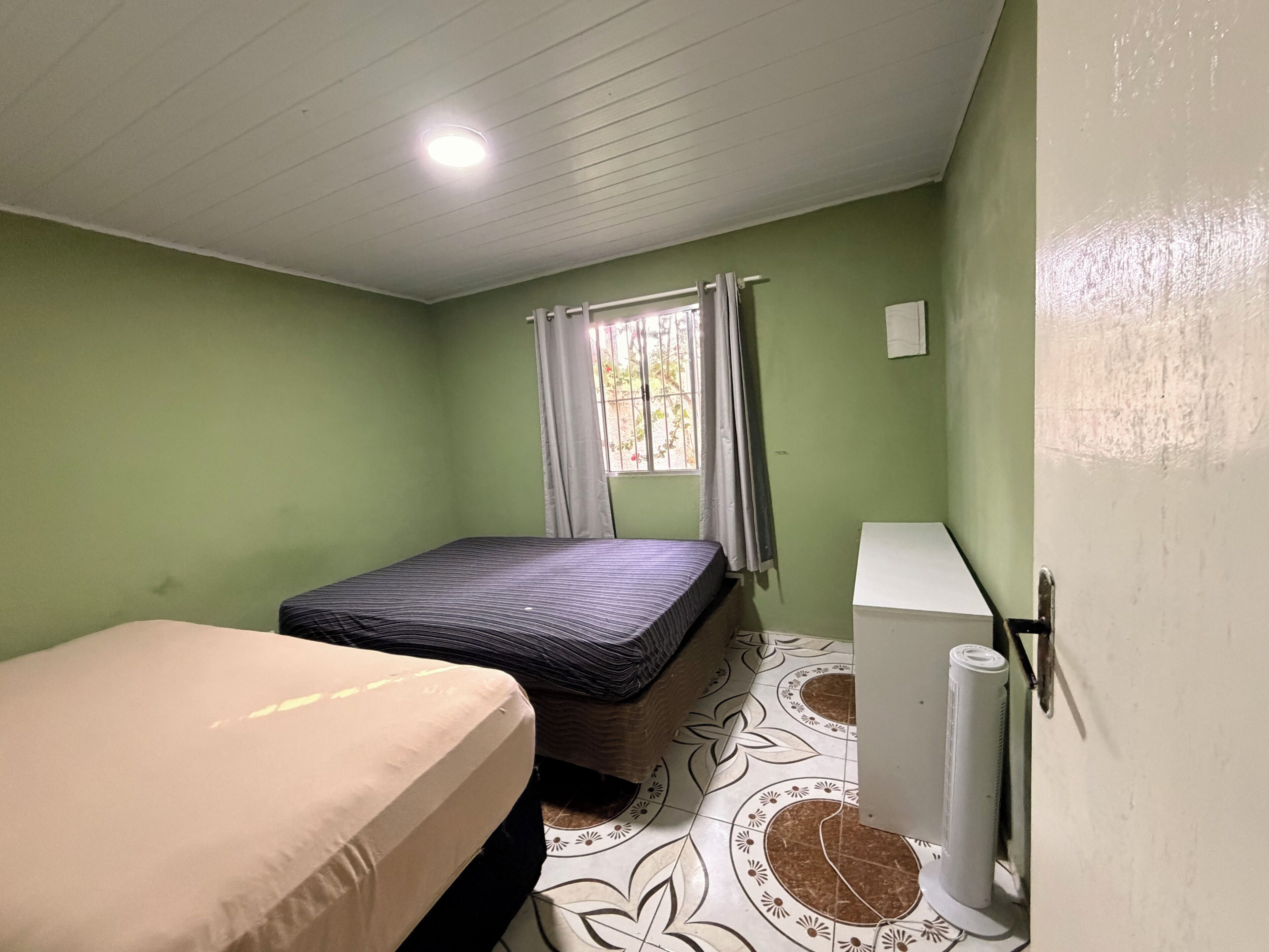 Een kamer met een bed, een raam met gordijnen, een radiator en een wandheater.