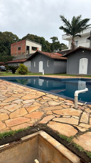 A swimming pool with stone tiles, a brick building, and a palm tree.