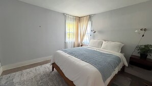 Un dormitorio con una cama, cortinas, una lámpara de techo y una planta en maceta.