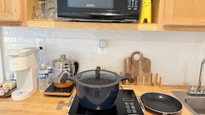 Una cocina con microondas, cafetera, estufa eléctrica, sartén y tabla de cortar de madera.