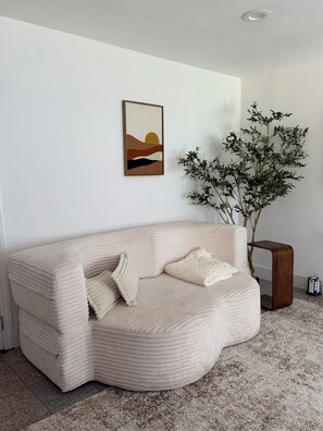 Una sala moderna con un sofá curvo, un cuadro abstracto enmarco y una planta en maceta.