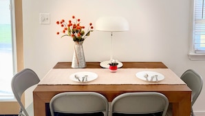 Una mesa de comedor con cuatro sillas, un florero con flores, una lámpara y una pequeña planta en maceta.