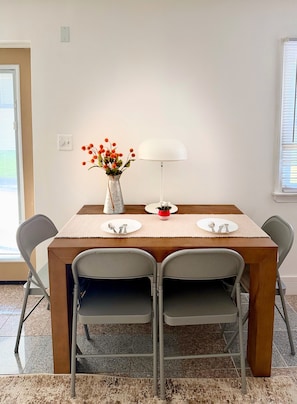 Et spisebord med fire stole, en vase med blomster, en lampe og en lille potteplante.