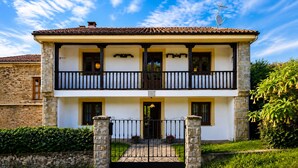 A two-story building with a balcony, a stone entrance gate, and a clear sky. - El Joyu Erías | House with a fenced-in garden in Llanes (Vidiago)