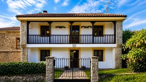 A two-story building with a balcony, a stone entrance gate, and a clear sky. - El Joyu Erías | House with a fenced-in garden in Llanes (Vidiago)