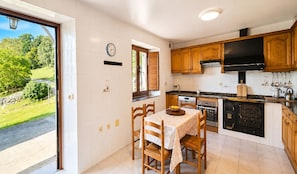 A kitchen with wooden cabinets, a stove, and a dining area with a table and chairs. - El Joyu Erías | House with a fenced-in garden in Llanes (Vidiago)