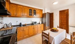 A kitchen with wooden cabinets, a microwave, a refrigerator, and a dining table with chairs. - El Joyu Erías | House with a fenced-in garden in Llanes (Vidiago)