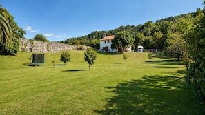A grassy field with a stone wall, a white building, and a red vehicle. - El Joyu Erías | House with a fenced-in garden in Llanes (Vidiago)