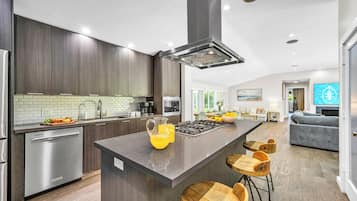 Une cuisine moderne avec des meubles en bois foncé, un lave-vaisselle en acier inoxydable et un îlot central doté de tabourets de bar.