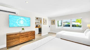 Une chambre moderne avec un grand téléviseur, une commode en bois, deux lits et une vue sur l’extérieur par la fenêtre.