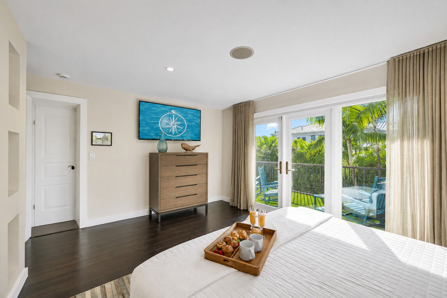 Une chambre avec un grand lit, une commode, un tableau et un balcon donnant sur un paysage verdoyant.