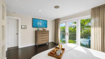 Une chambre avec un grand lit, une commode, un tableau et un balcon donnant sur un paysage verdoyant.