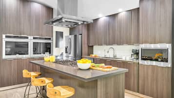Une cuisine moderne dotée d’un îlot central, d’appareils électroménagers en acier inoxydable et de tabourets de bar en bois.