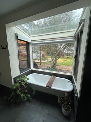 Ein Badezimmer mit Badewanne, einem Fenster und einer Topfpflanze.