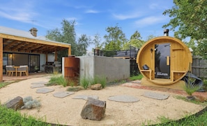 Eine rustikale Außenanlage mit einer Holzsauna, einem Grillbereich und einer überdachten Sitzgelegenheit.