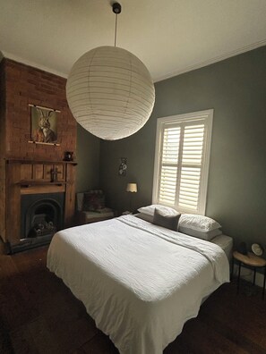 Een slaapkamer met een groot bed, een open haard, een hanglamp en een raam met blinds.