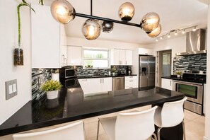 A modern kitchen with a central island, stainless steel appliances, and a black countertop. - Luxury Hollywood Beach House , 4BR/2BA, Private Pool, Sleeps 8, 5 Min to Beach (Hollywood)