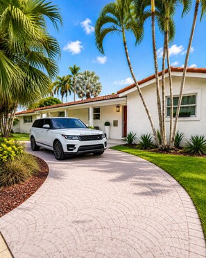 A white Range Rover parked in front of a house with a curved driveway, surrounded by palm trees and a clear blue sky. - Luxury Hollywood Beach House , 4BR/2BA, Private Pool, Sleeps 8, 5 Min to Beach (Hollywood)