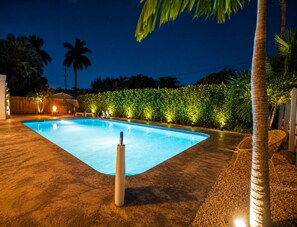 Ein Pool mit Whirlpool, umgeben von Palmen und einem Hecken.