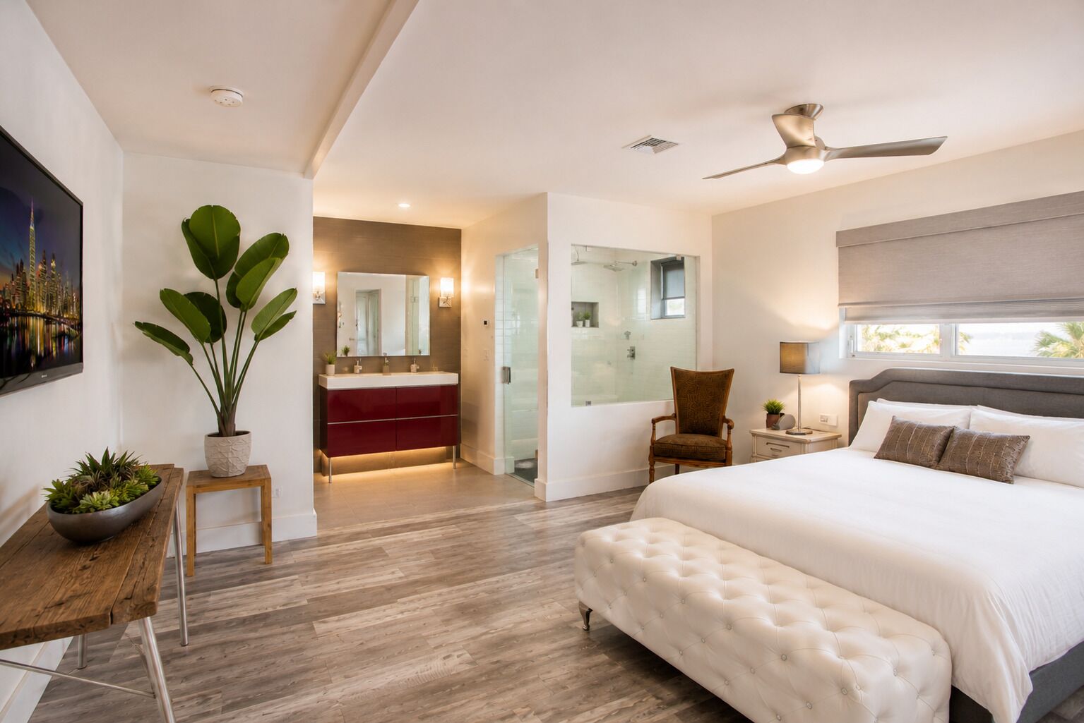 A modern bedroom with a large bed, a sitting area with a chair, a small table, and a potted plant.