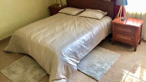 A neatly made bed with a white duvet, two bedside tables with lamps, a wooden nightstand, and a light-colored rug on a tiled floor. - AriCo is your home away from home in Cochabamba. 🏡 (Cochabamba)