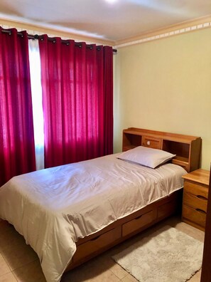 Ein Einzelbett mit Holz-Kopfteil, ein Nachttisch und ein roter Vorhang.
