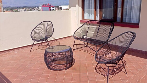 A terrace with two chairs and a small round table, a window with curtains, and a view of buildings in the distance. - AriCo is your home away from home in Cochabamba. 🏡 (Cochabamba)