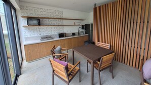 Eine moderne Küche mit integriertem Mikrowellenherd, Toaster und Spüle. Ein Esstisch mit Stühlen und eine Holzwand sind vorhanden.