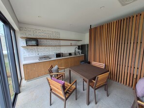 Eine moderne Küche mit integriertem Mikrowellenherd, Toaster und Spüle. Ein Esstisch mit Stühlen und eine Holzwand sind vorhanden.