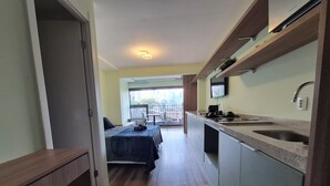 Ein schmaler Flur führt zu einem Balkon mit einem Bett und einer Küchenzeile, die ein Spülbecken und einen Fernseher beinhaltet.