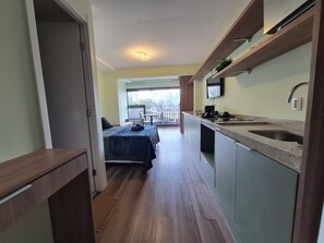 Ein schmaler Flur führt zu einem Balkon mit einem Bett und einer Küchenzeile, die ein Spülbecken und einen Fernseher beinhaltet.
