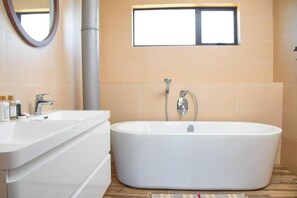 Un bagno moderno con una vasca freestanding, un lavabo con specchio e una finestra sopra la vasca.